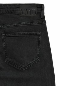 Poche arrière d'un jean en denim noir avec des coutures visibles et un patch en cuir noir embossé de "VVD" sur la ceinture.
