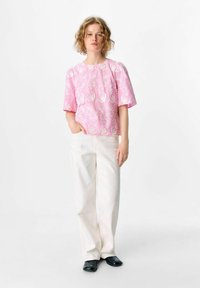 Blouse rose à manches courtes avec broderies florales blanches, assortie à un pantalon droit blanc et des chaussures plates noires. Design minimaliste, coupe décontractée.