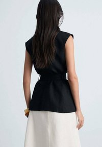 Top corto nero a maniche corte con vita cintrata, tessuto testurizzato, taglio cropped, abbinato a una gonna fluida di colore chiaro.