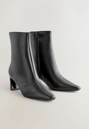 Juodos odinės aulinukai iki kulkšnies su smailiu nosiu, blokuotu kulnu ir šonine užtrauktuku. Lygi tekstūra su elegantišku dizainu, kuris suteikia prigludusią išvaizdą.