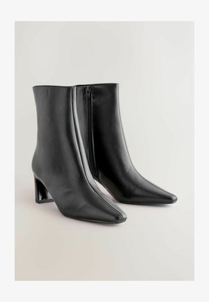 Black leather ankle boots with a pointed toe, block heel, and side zipper. Smooth texture with a sleek design for a fitted look.