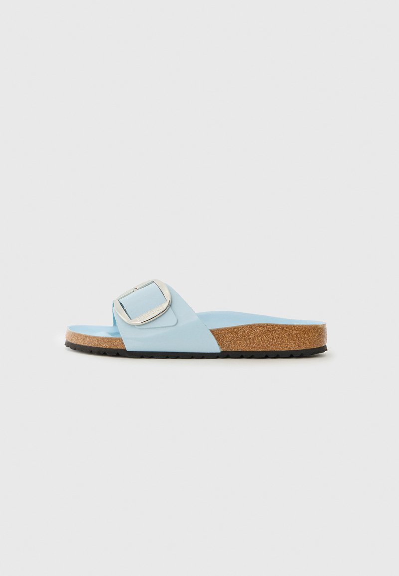 Sandal de slide azul com uma faixa larga, apresentando uma grande fivela prateada. Palmilha em cortiça e sola exterior em borracha preta para aderência e conforto.