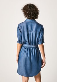 Denim shirt dress with a cinched waist, short sleeves, and a curved hem. Features a button-down collar and a smooth, lightweight texture.