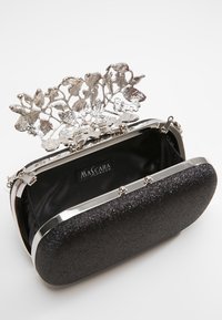 Svart glittrande kuvertväska med silvrig metallblomklämma och ram, öppen för att visa insidan av svart tyg märkt "Mascara London."