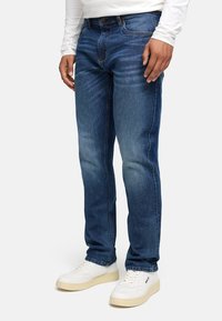 Tynne blå denimjeans med en falmet vask, fem-lommers design og knappelukking, kombinert med hvite sneakers.