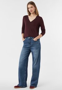Bordeaux lange mouwen top met een V-hals, gecombineerd met wijde blauwe jeans. De outfit heeft een ontspannen pasvorm en een klassieke denim textuur.