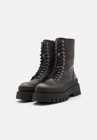 Black leather combat boots with a chunky platform sole, flat laces, and metal eyelets. Features a round toe and side zipper detail.