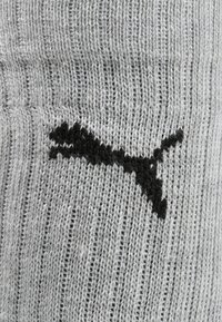 Graue gestrickte Socke mit einem strukturierten Muster und dem schwarz aufgedruckten Puma-Logo. Das Material ist weich und hat gerippte Details.
