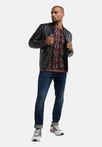 Veste en cuir noire sur une chemise à motifs rouge, blanche et noire, accompagnée de jeans bleus et de baskets multicolores.