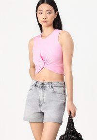 Roosa lühike top, mille esiküljel on keerdus detail, koos heledate hallide denimpüksega, millel on kõrge vöökoht ja üleskeeratud servad. Hoides musta lillemustriga kotti.
