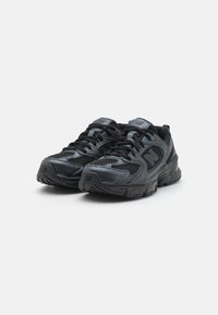 Baskets de sport noires avec tige en mesh et synthétique, col rembourré, lacets et semelle en caoutchouc texturé, avec un logo sur la languette.