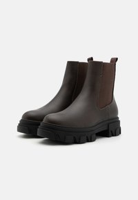 Bottes de cheville en cuir marron avec des panneaux élastiques sur les côtés et une épaisse semelle en caoutchouc noir. Présentent un bout rond et des détails de couture contrastants.