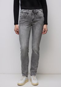 Grå denimjeans med smal passform, som har midja i midjehöjd, framfickor och subtilt solkigt utseende. Kombinerade med vita sneakers.