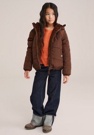 Veste rembourrée marron avec un doublure en fausse fourrure, portée sur un pull orange. Jeans noirs avec des poignets contrastants et des chaussures à motifs léopard.