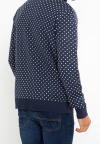 Marineblauer Strickpullover mit einem weißen Rautenmuster. Gerippte Bündchen und Saum mit lockerer Passform. Sichtbare Nähte.