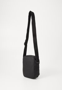 Borsa a tracolla in pelle nera di forma quadrata, con tracolla regolabile, texture liscia e chiusura con zip. Design semplice e minimalista.