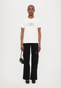 White short-sleeve t-shirt featuring a rhinestone logo. Paired with black cargo pants and a small black handbag. Black flats with accents.
