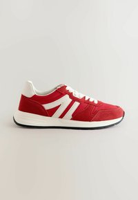 Pantof de sport roșu, cu superior din piele suede, accente albe și șireturi plate albe. Prezintă o talpă din cauciuc texturat și un călcâi neted.