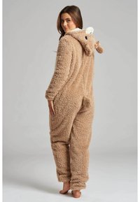 Bruine pluche onesie met een capuchon, voorzien van dierenoren en een donzige afwerking. Het heeft elastische manchetten en een staartdetail aan de achterkant.
