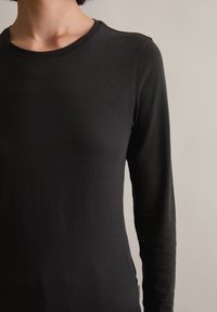 Czarna koszulka z długim rękawem wykonana z miękkiego materiału, z okrągłym dekoltem, o dopasowanym kroju i minimalnych szwach, co zapewnia schludny wygląd.