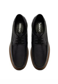 Chaussures en cuir noir avec tige texturée, bout rond, laçage à six œillets et semelle en caoutchouc marron. Nom de la marque "DERMOD" visible sur la semelle intérieure.