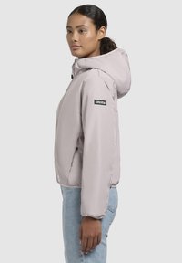 Light pink padded jacket with a hood, featuring a black logo on the left arm, elastic cuffs, and a compact design. Worn with light blue jeans.