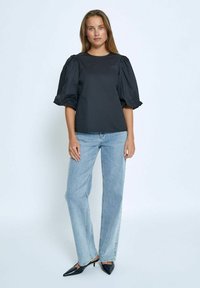 Top nero con maniche a palloncino in tessuto liscio, abbinato a jeans dritti azzurri e tacchi neri con punta affilata. Design semplice e moderno.