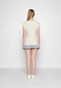 Camiseta bege clara de mangas curtas, combinada com uma saia de ganga azul clara em camadas e ténis brancos. Design simples e casual.