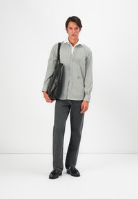 Stripet skjorte med knapper i hvit og svart, parret med mørkegrå jeans og svarte loafers, bærende en svart skinn totebag.