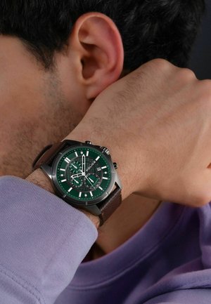 Montre chronographe avec un cadran vert, des index argentés et un bracelet en cuir marron. Présente un motif texturé et une fenêtre de date.