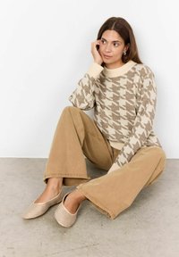 Beež houndstooth-mustri salliga sviiter, mis on kombineeritud beežide laia säärega pükstega ja tekstuursete sussidega.