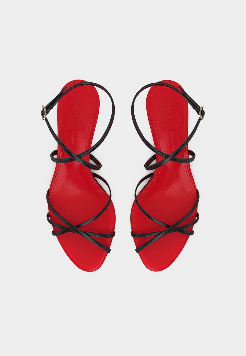 Rote flache Sandalen mit dünnen schwarzen gekreuzten Riemen und Knöchelriemen mit Schnallen, von oben auf hellem Hintergrund gezeigt.