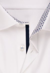 Witte shirt met een marineblauwe contrast inzet en een patroon op de kraag. Heeft een knoop met een blauwe draad detail, wat een nette, op maat gemaakte uitstraling geeft.