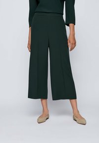 Gröna vida byxor med slät textur, med hög midja och veck. Kombination med neutrala lägenheter.