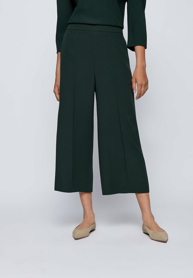 Gröna vida byxor med slät textur, med hög midja och veck. Kombination med neutrala lägenheter.