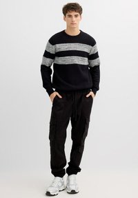 Suéter azul marino con tejido texturizado y rayas horizontales grises, combinado con pantalones cargo negros con múltiples bolsillos y zapatillas blancas.