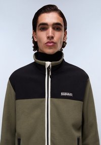 Giacca in pile nera e verde con colletto alto, zip bianca e patch con logo. Tessuto morbido e design color-block con tasche laterali.