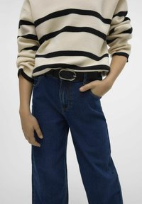 Pull rayé noir et crème avec des manches retroussées, associé à un jean bleu foncé, coupe ample. Ceinture en cuir noir avec une boucle ovale en argent.