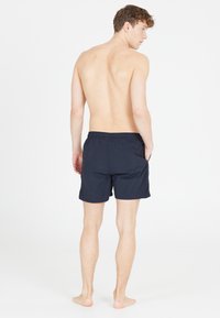 Marinblå badshorts med elastisk midja och sidofickor, tillverkade av lätt material, visade bakifrån.