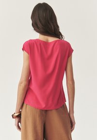 Fuchsia bluse med korte ærmer, blød tekstur og rund halsudskæring. Kombineret med lysebrune brede bukser. Glat, draperende stof.