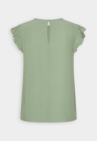 Blouse vert clair à coupe décontractée, avec de courtes manches à volants et une fermeture en forme de trou de serrure à l'arrière. Texture douce avec des détails minimaux.