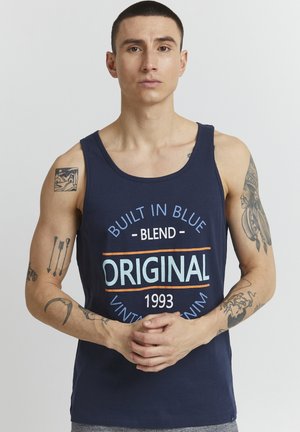 Mørkeblå tank top med rund halslinning, prydet med flerfarget trykk: "BYGGET I BLÅTT - BLEND - ORIGINAL 1993" mot en ensfarget bakgrunn.