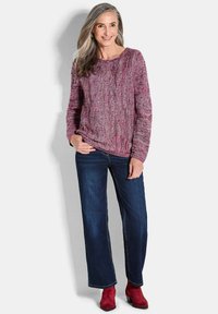 Pullover lavorato a maglia in tonalità di bordeaux e rosa, caratterizzato da un motivo a trecce testurizzato. Abbinato a jeans blu scuro e stivaletti rossi.