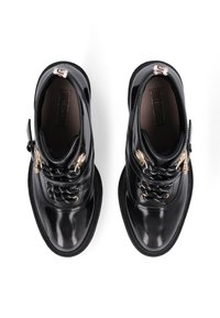 Schwarze Lacklederstiefel mit Gummisohlen, metallischen Ösen, schwarz-weißen Schnürsenkeln, runder Lasche und einem weich strukturierten Innenfutter.