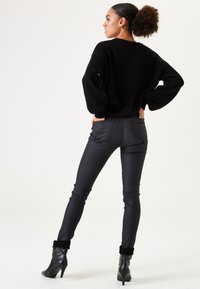 Schwarzer gerippter Strickpullover mit übergroßen Ärmeln, kombiniert mit eleganten schwarzen Kunstlederhosen mit Gesäßtaschen und knöchellangem Schnitt.