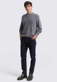 Grijze pullover met een ronde hals, gecombineerd met donkerblauwe spijkerbroeken. Model draagt zwarte enkellaarsjes met een gestructureerde zool.