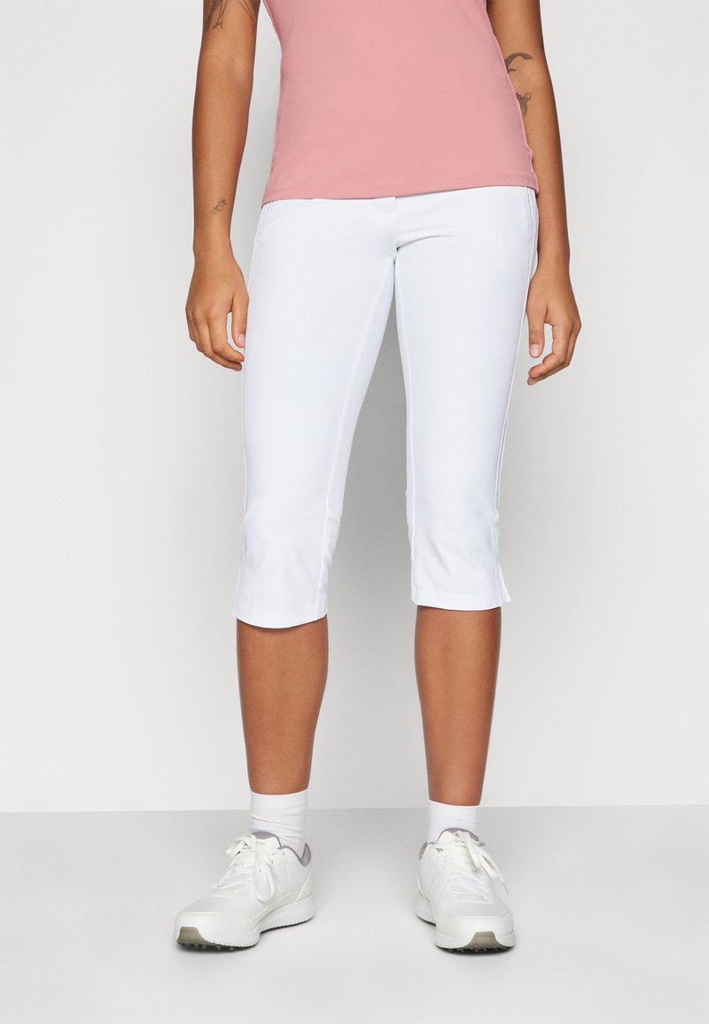 Pantalones capri blancos hechos de tela elástica, con un diseño ajustado, dobladillo a la altura del tobillo y cinturilla plana. Combinados con una camiseta rosa y zapatillas blancas.