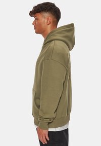 Felpa con cappuccio verde oliva con tasca a marsupio, polsini a coste e cappuccio con coulisse. Tessuto morbido con dettagli minimali di cucitura.