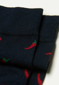 Marineblå sokker med et gentaget mønster af røde chili pebre med grønne accenter, som fremviser en blød strikstruktur og ribbede manchetter.