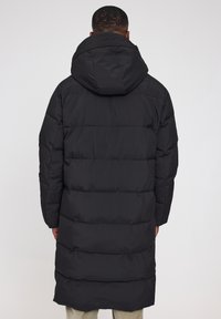 Schwarze Pufferjacke mit Kapuze, mit gestepptem Design und langer Länge. Das Material wirkt isoliert und hat eine glatte Textur.